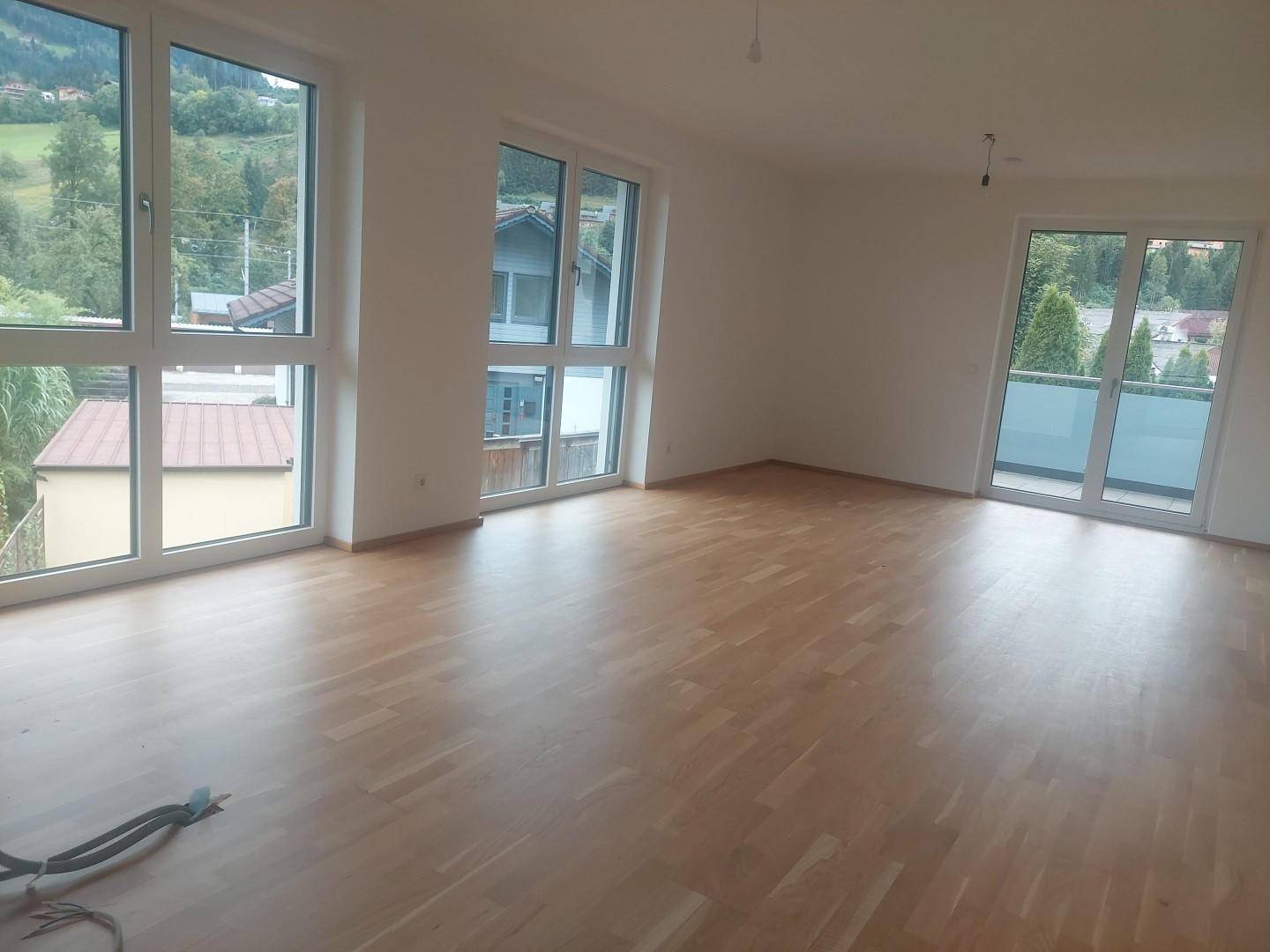 Heller Wohnraum mit großen Fenstern, Holzboden und Blick auf die umliegende Landschaft.