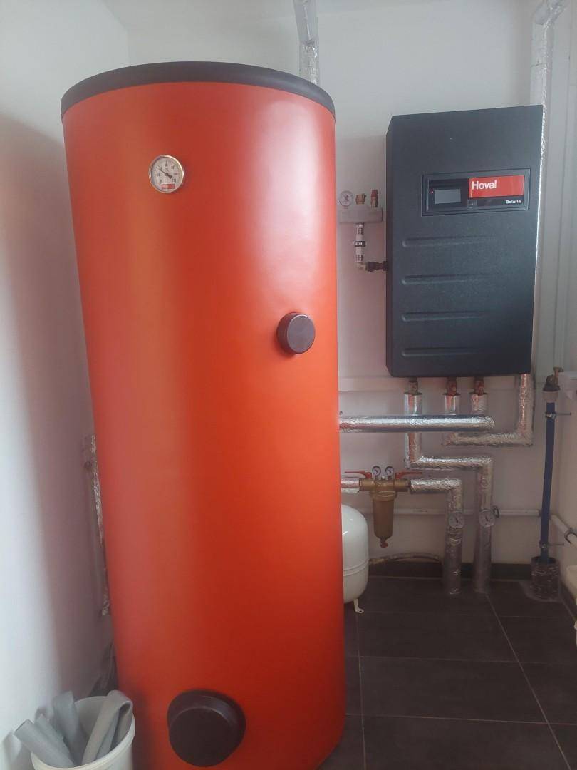 Heizungsraum mit großem Warmwasserspeicher und Steuerungseinheit an der Wand.