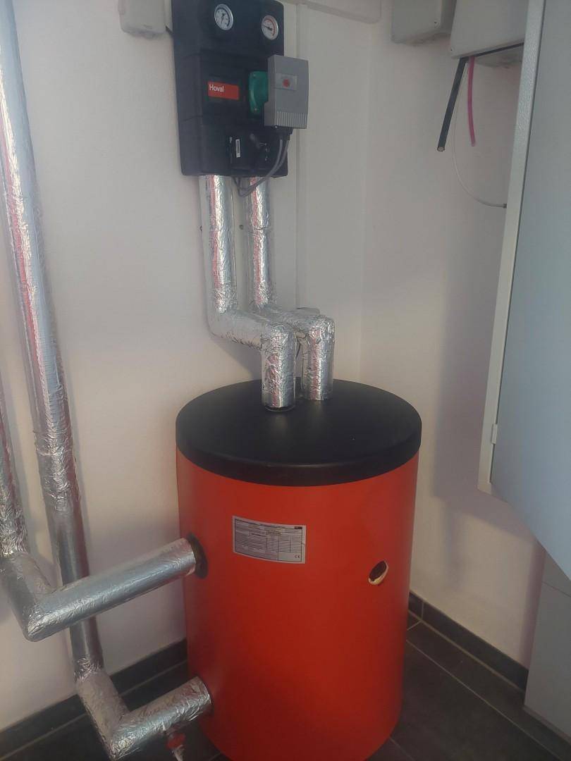 Technikraum mit Warmwasserspeicher und isolierten Rohren, sauber installiert.