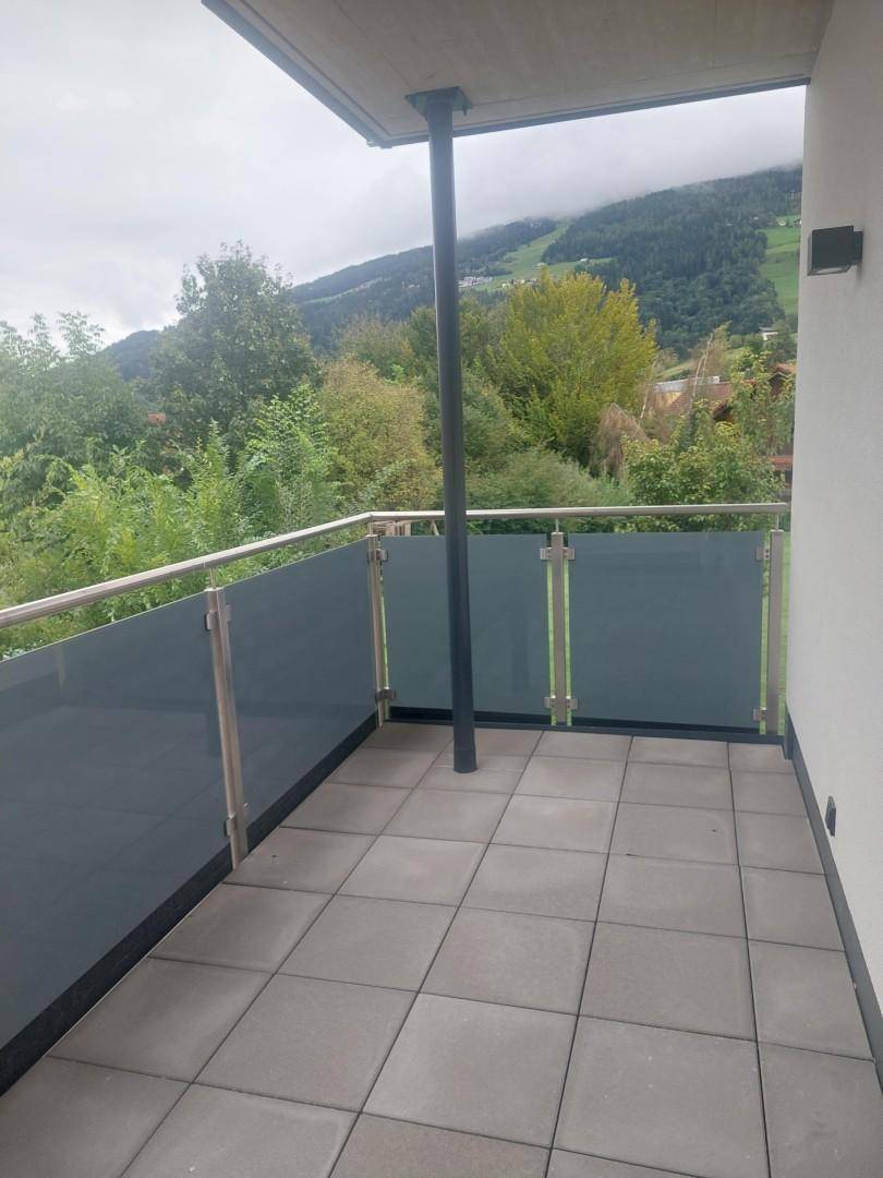 Moderner Balkon mit Fliesenboden und Glasbrüstung, bietet einen weiten Blick auf die umliegende Berglandschaft.