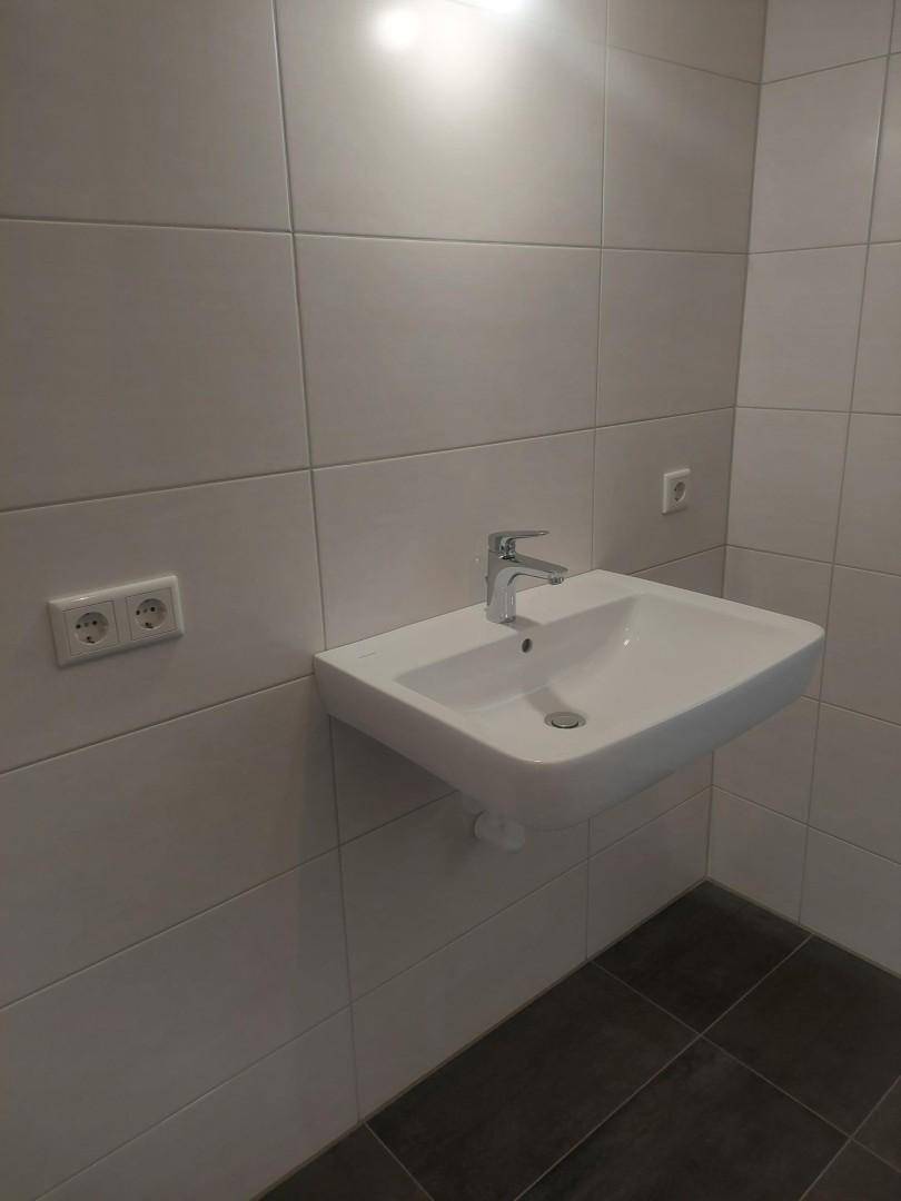 Modernes Badezimmer mit weißem Waschbecken, hellen Wandfliesen und dunklem Boden.