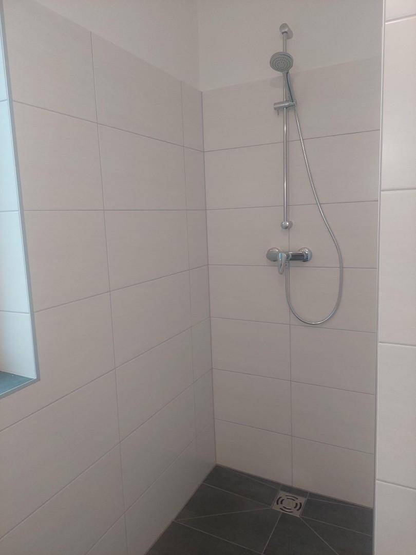Duschbereich im modernen Badezimmer mit hellen Wandfliesen und dunklem Boden, ausgestattet mit einer Handbrause.