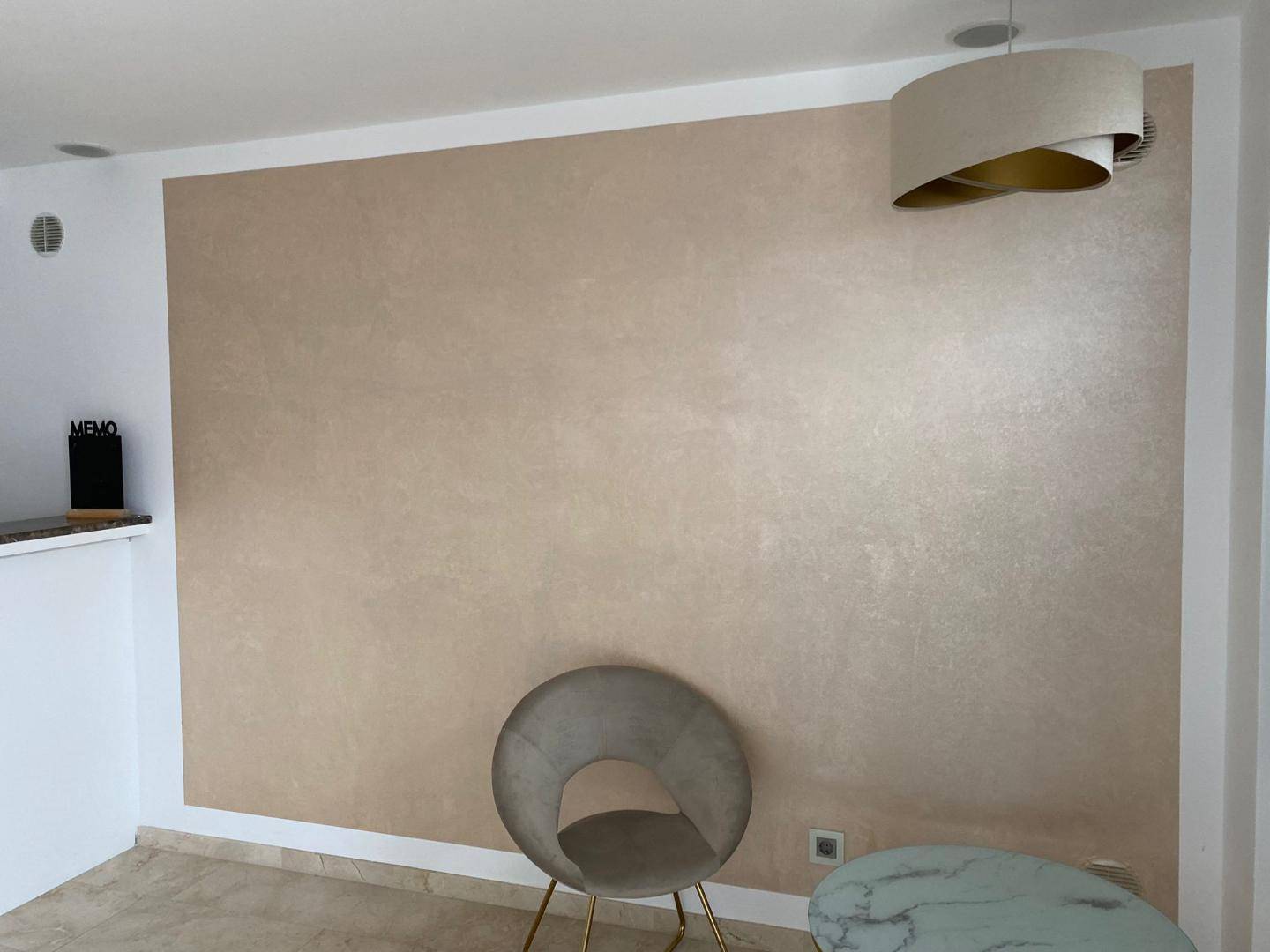 Heller Raum mit einer beigefarbenen Akzentwand, modernem Stuhl und stilvoller Deckenleuchte.