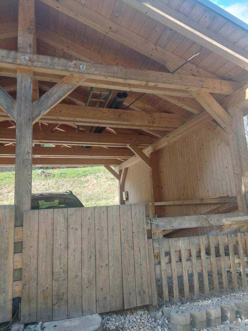 Offener Holzcarport mit sichtbaren Balken und einem geparkten Auto im Hintergrund.