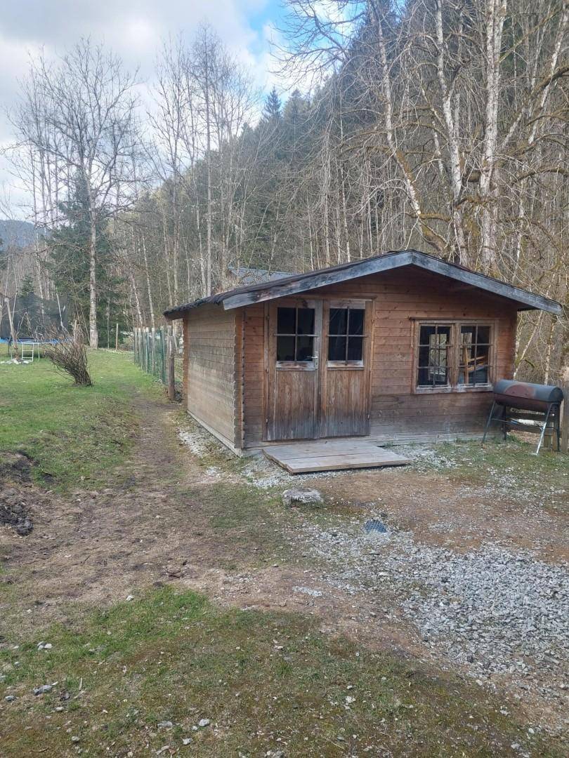 Kleiner Holzschuppen mit Fenstern und einer Grillstation in ländlicher Umgebung.