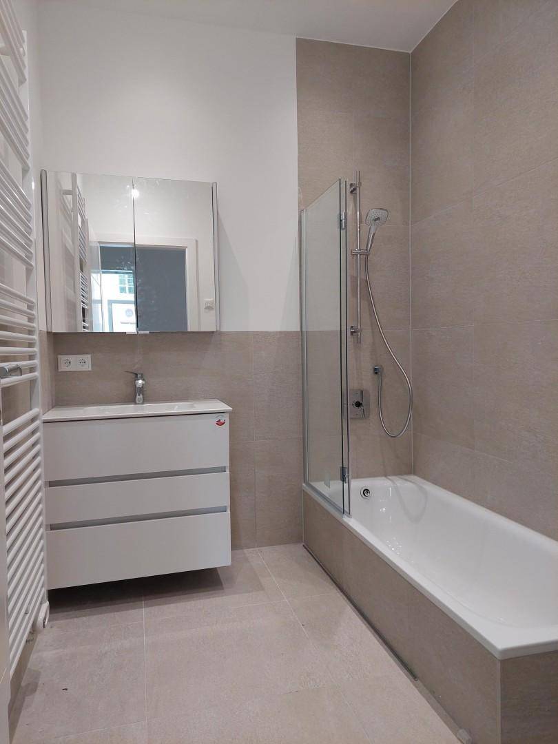 Modernes Badezimmer mit Badewanne, Duschabtrennung, Waschtisch und beheiztem Handtuchhalter.