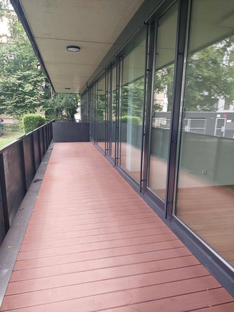 Lange Terrasse mit Holzbelag und großen Glasfronten, die den Innenraum mit dem Außenbereich verbinden.