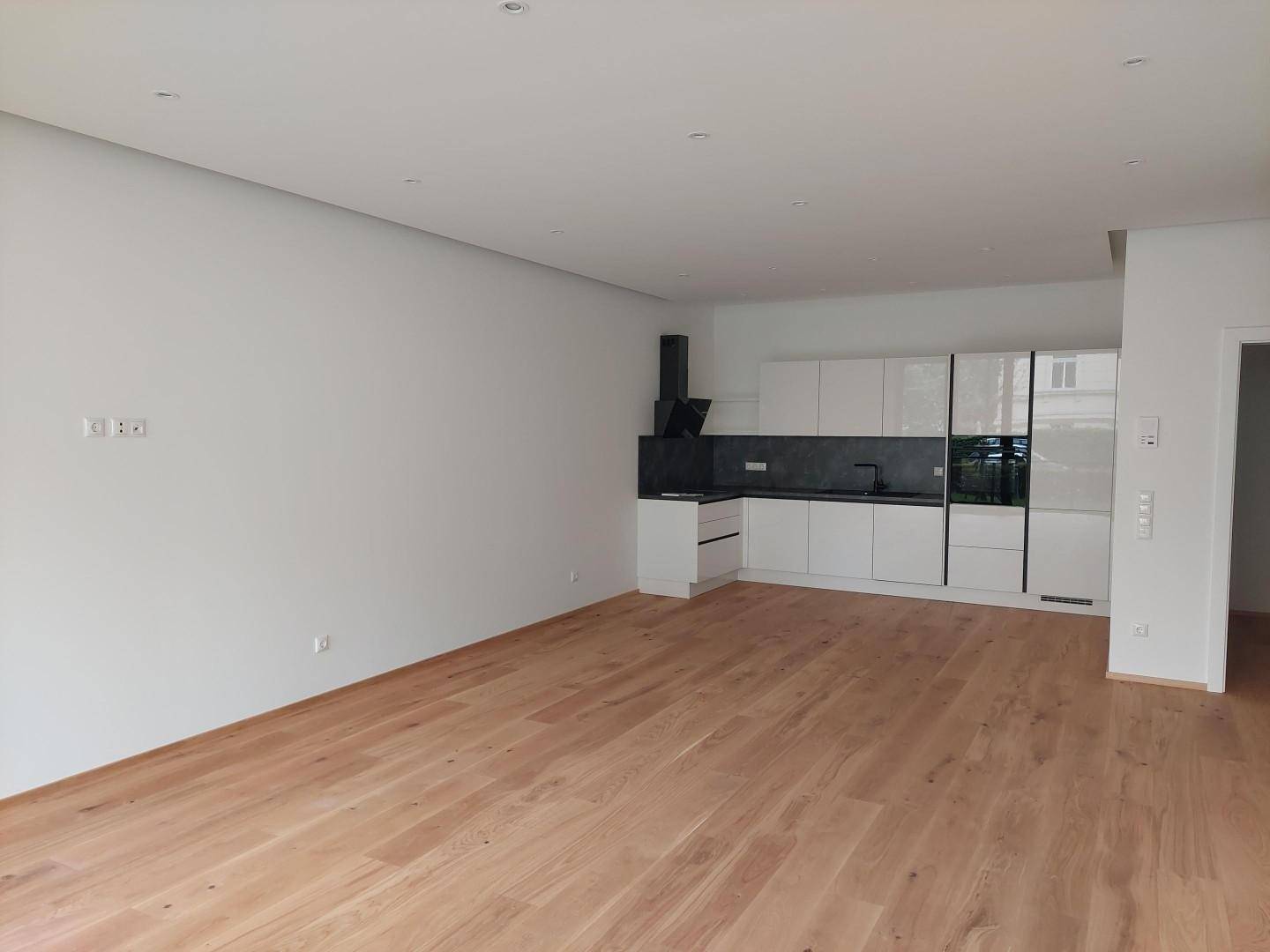 Offener Wohnbereich mit moderner Einbauküche, Holzboden und weißen Schränken.