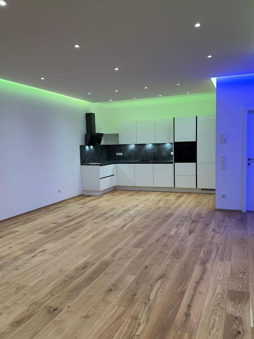 Moderne Einbauküche in einem offenen Wohnbereich mit Holzboden und farbiger LED-Deckenbeleuchtung.