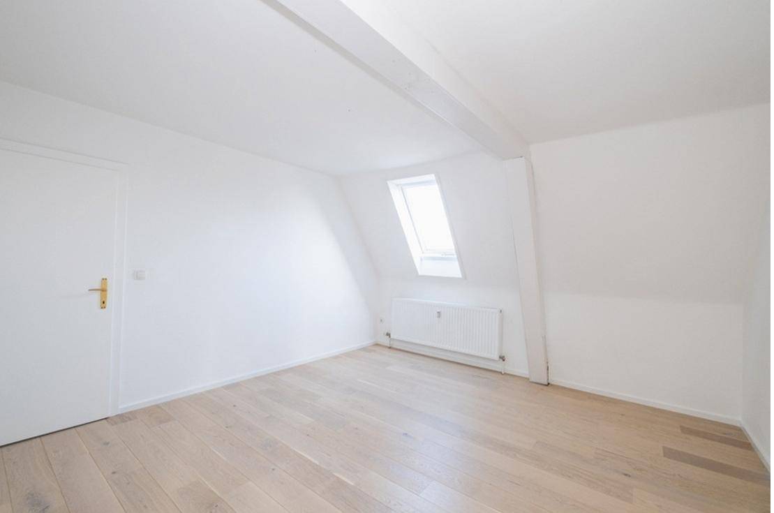 Helles Zimmer im Dachgeschoss mit Holzboden, Dachfenster und schrägen Wänden.