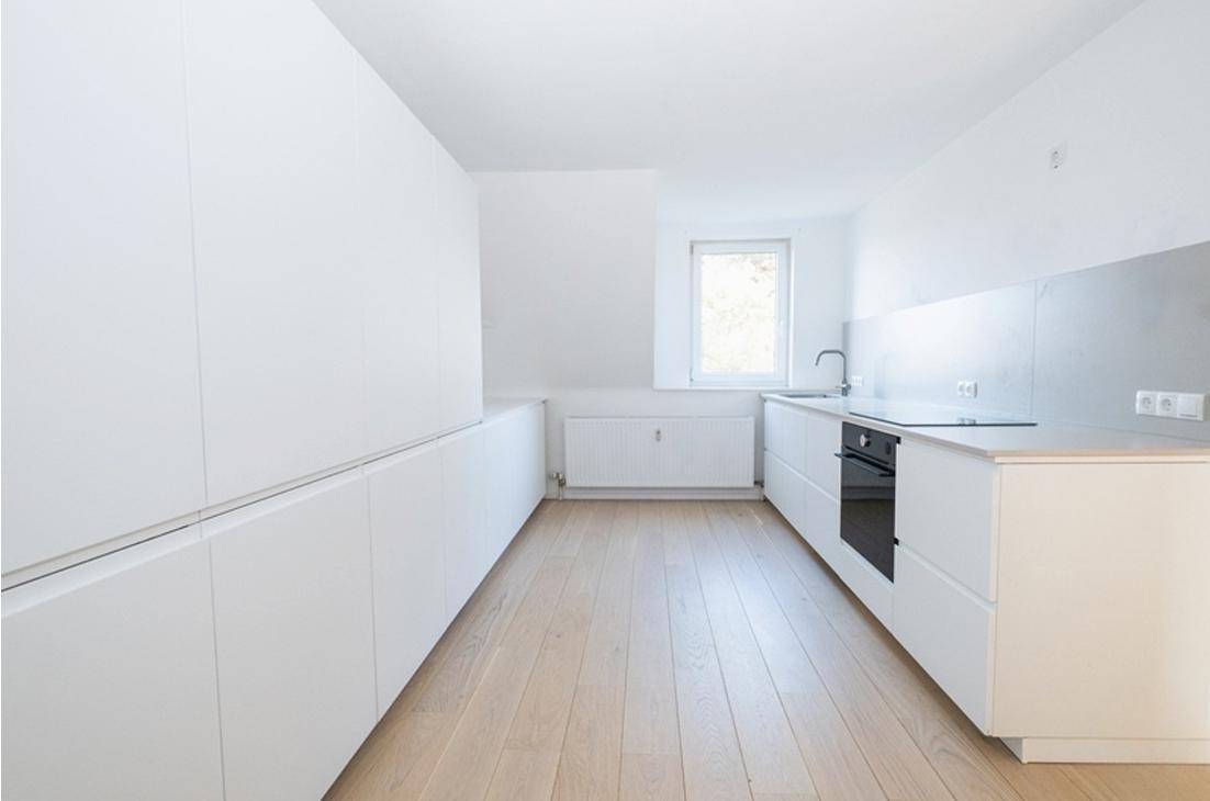 Helle, moderne Küche mit weißen Schränken, Holzboden und integrierten Geräten.