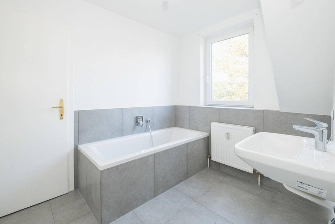 Modernes Badezimmer mit Badewanne, Waschbecken und grauen Fliesen an Wand und Boden.