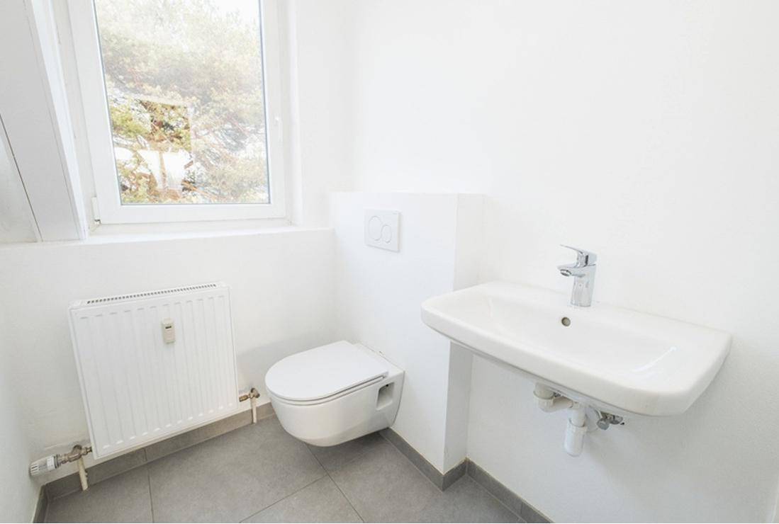 Kleines WC mit wandhängender Toilette, Waschbecken und Fenster für Tageslicht.