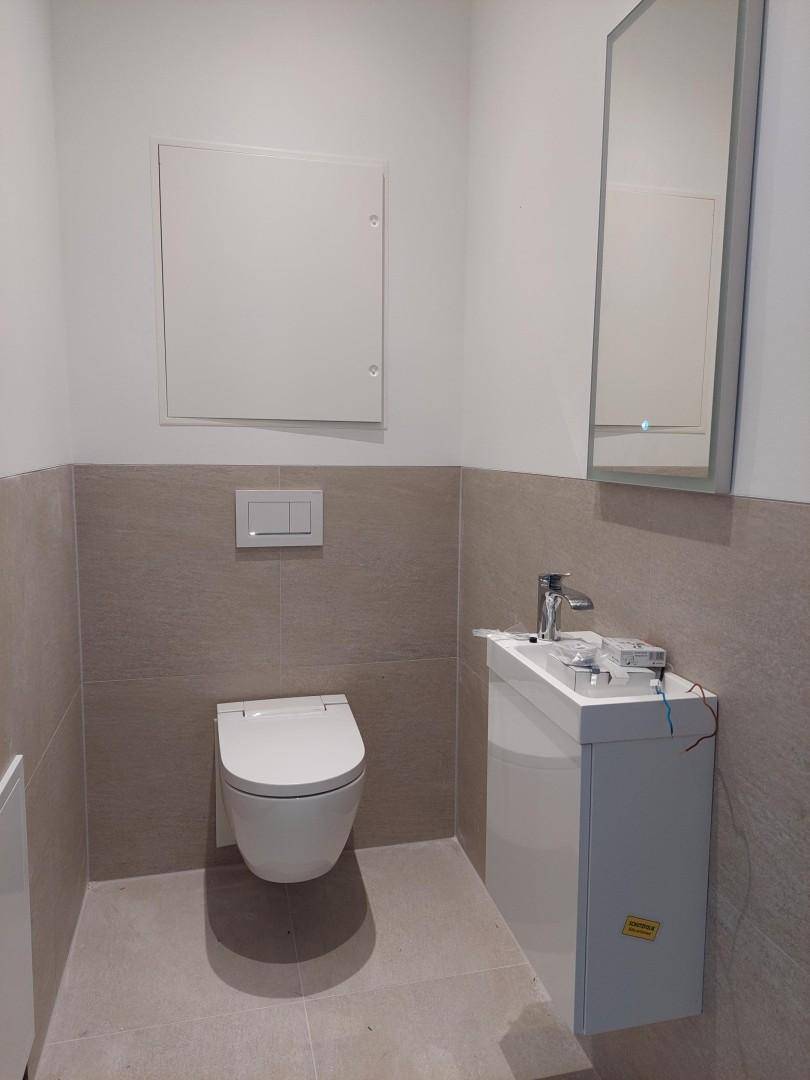 Modernes Gäste-WC mit wandhängender Toilette, kleinem Waschbecken und beigefarbenen Fliesen.