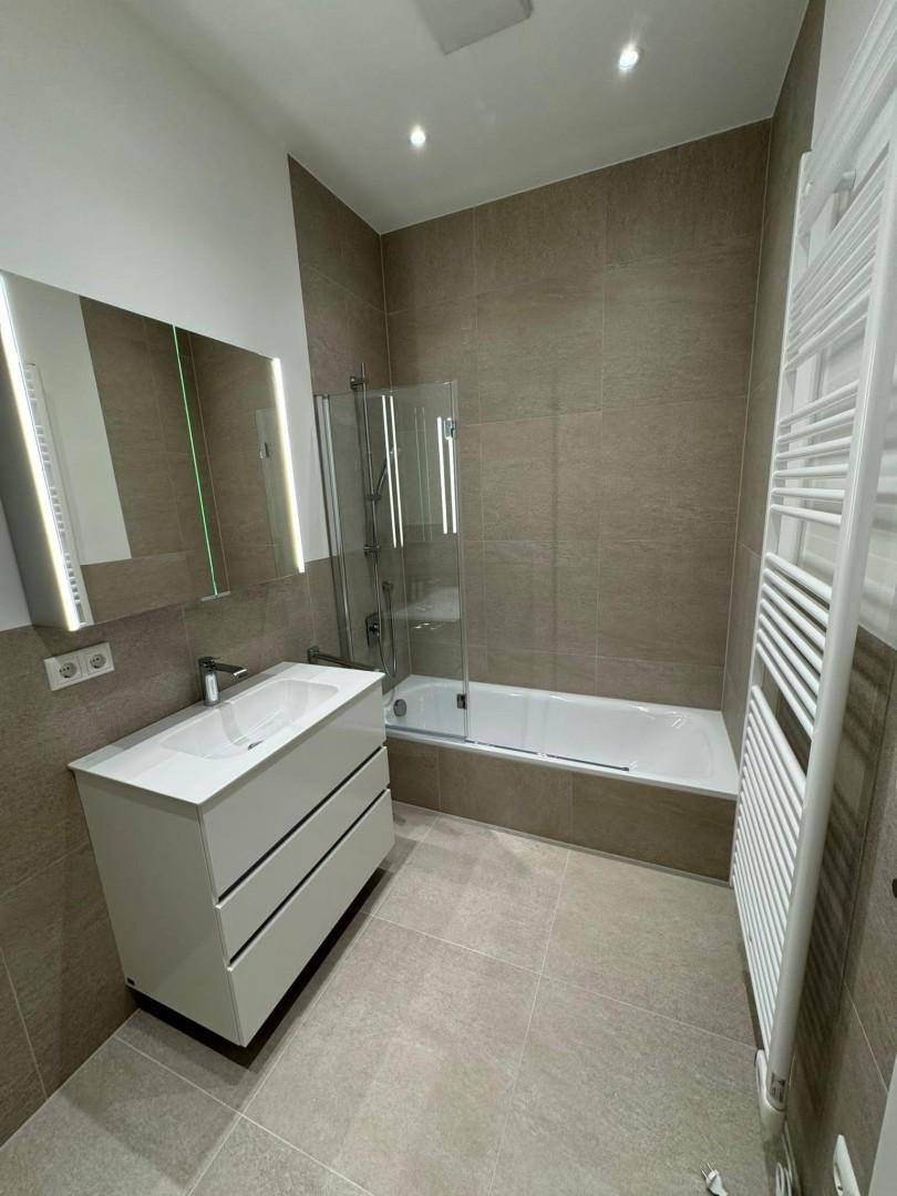 Modernes Badezimmer mit Badewanne, Duschabtrennung, großem Waschtisch und beheiztem Handtuchhalter.
