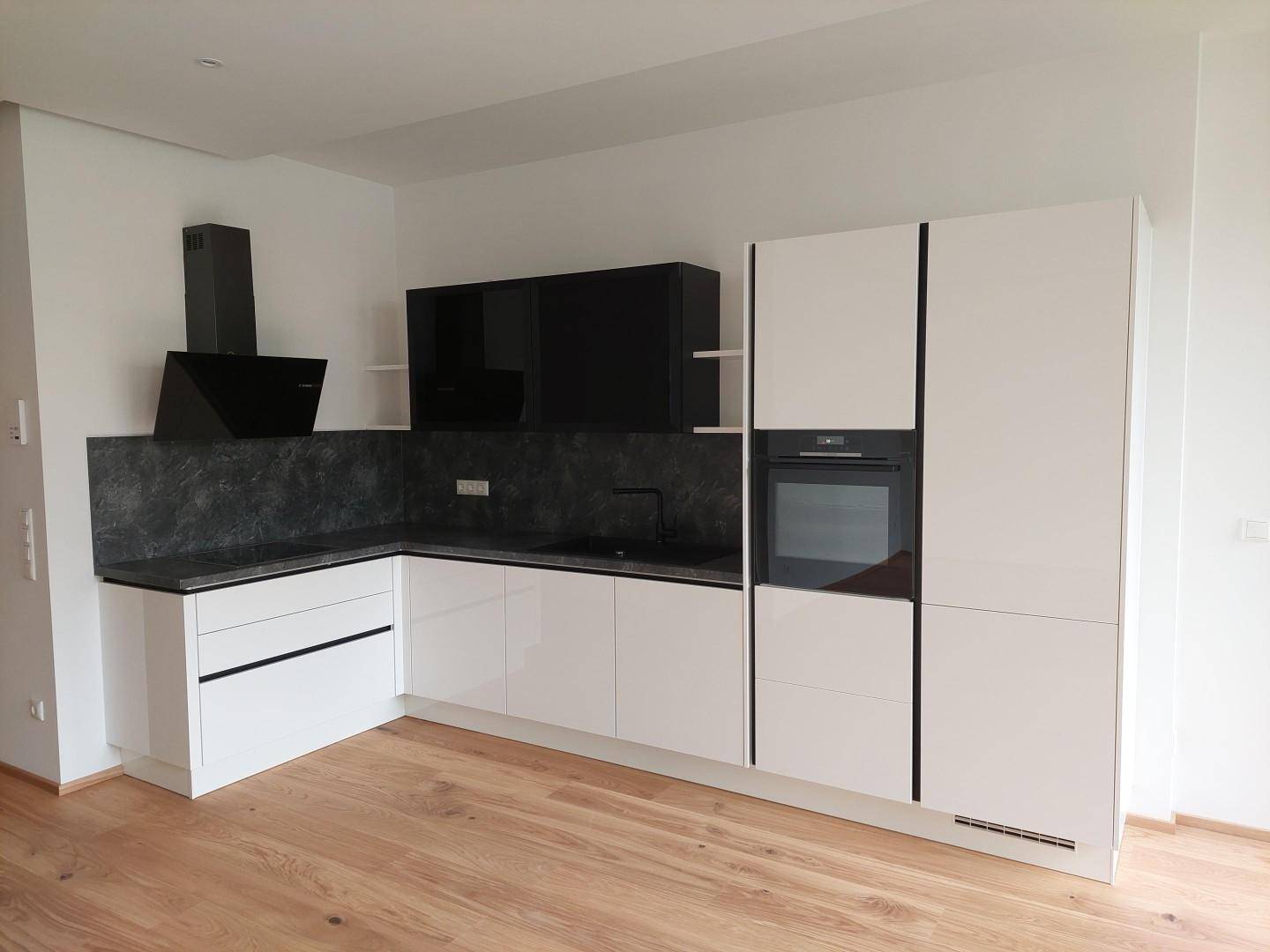 Moderne Einbauküche mit weißen Hochglanzfronten, dunkler Arbeitsplatte und integrierten Elektrogeräten.