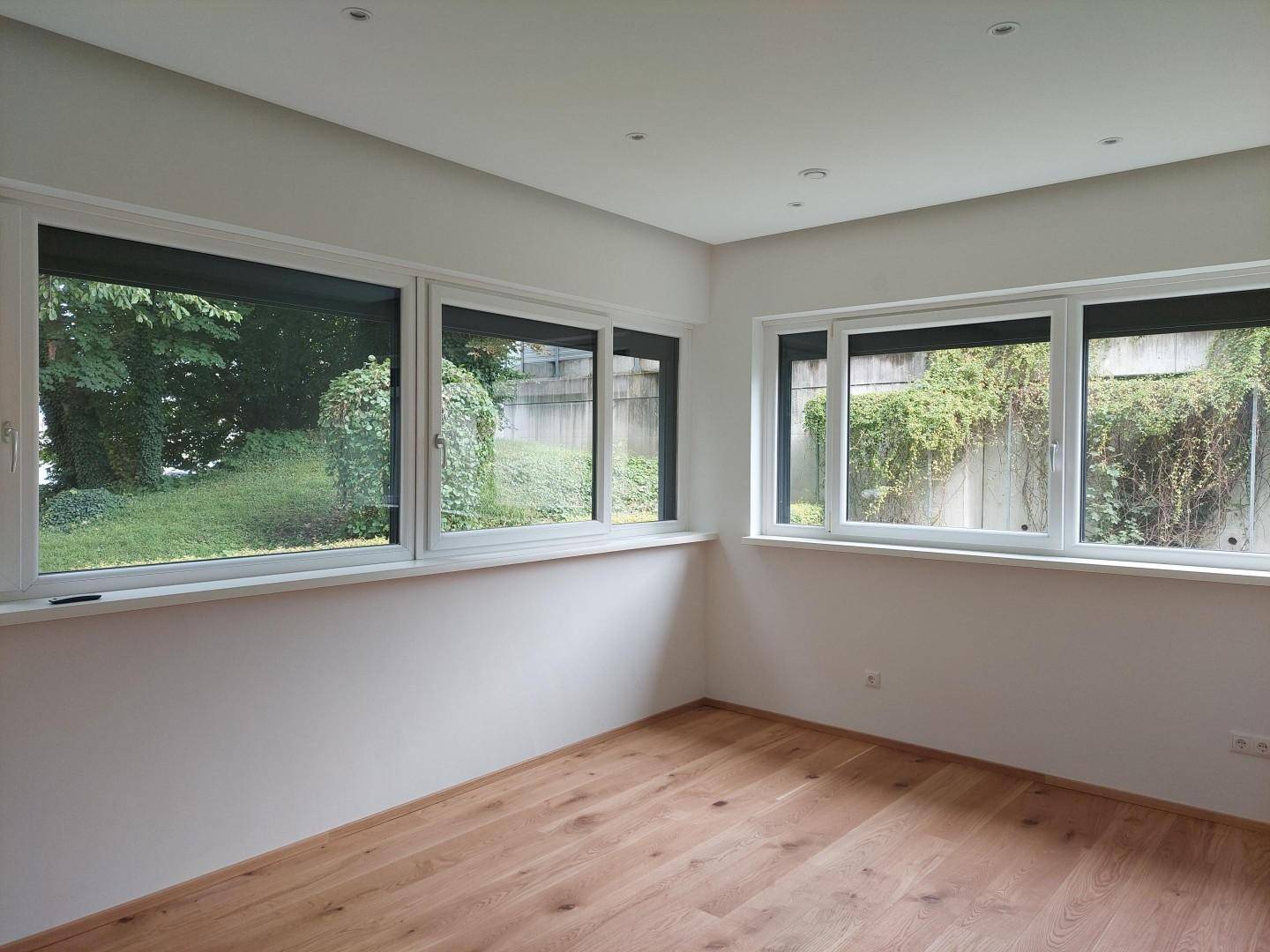 Geräumiges Zimmer mit Parkettboden und mehreren Fenstern, die viel Tageslicht hereinlassen.