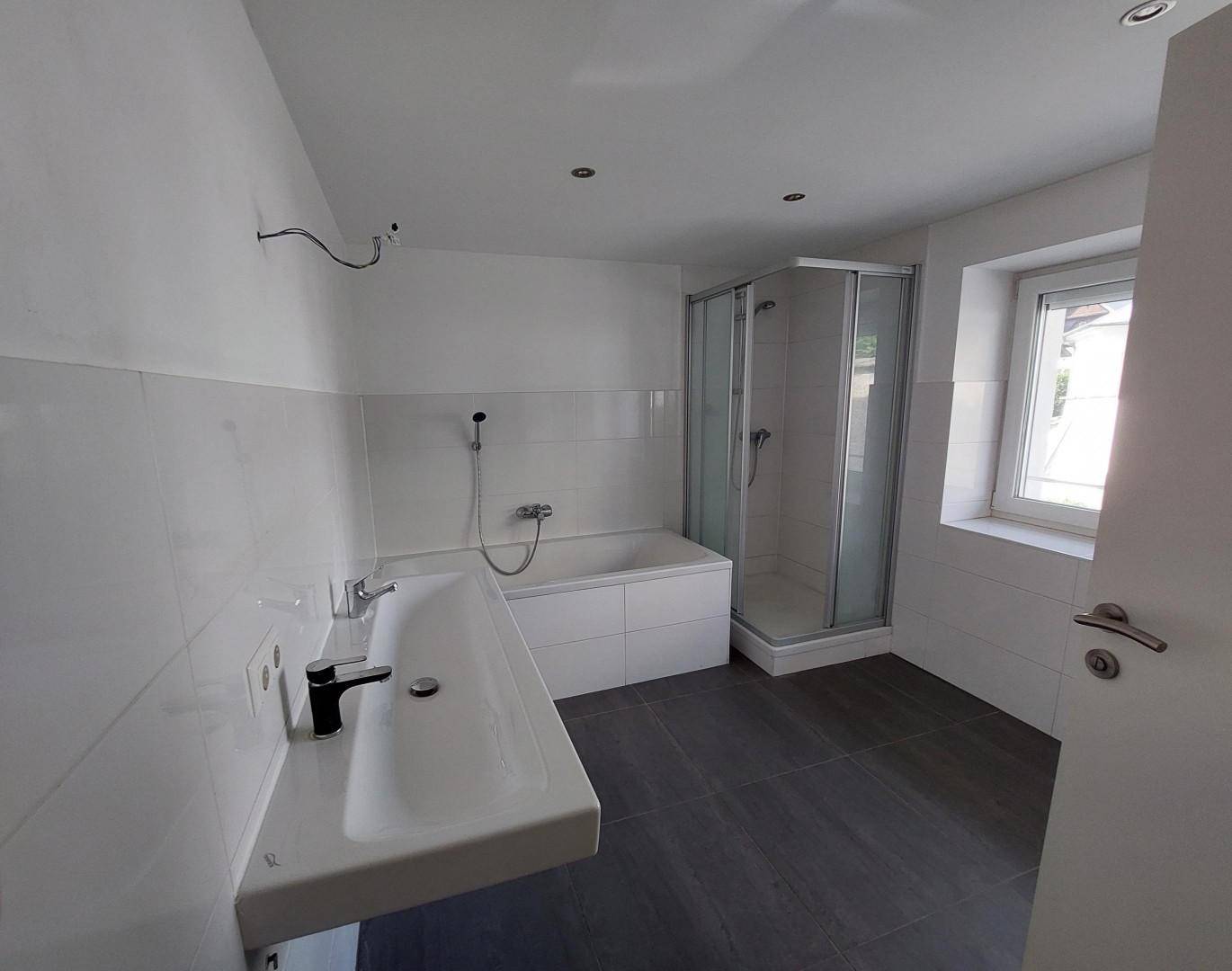 Modernes Badezimmer mit Badewanne, Duschkabine, Waschbecken und Fenster.