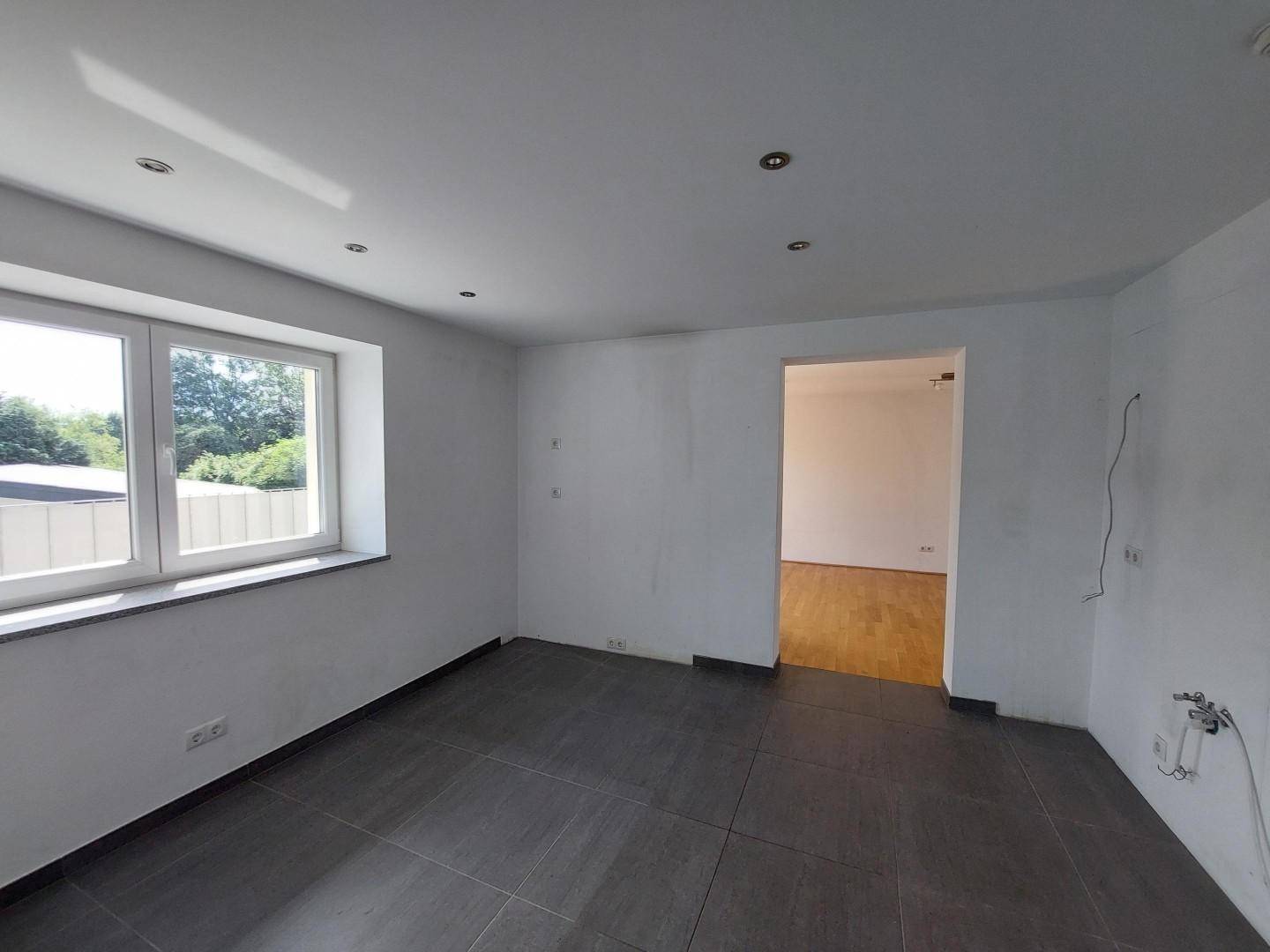 Leerer Raum mit dunklen Fliesen, Fenster und Anschlussmöglichkeiten für eine Küche oder Waschküche.