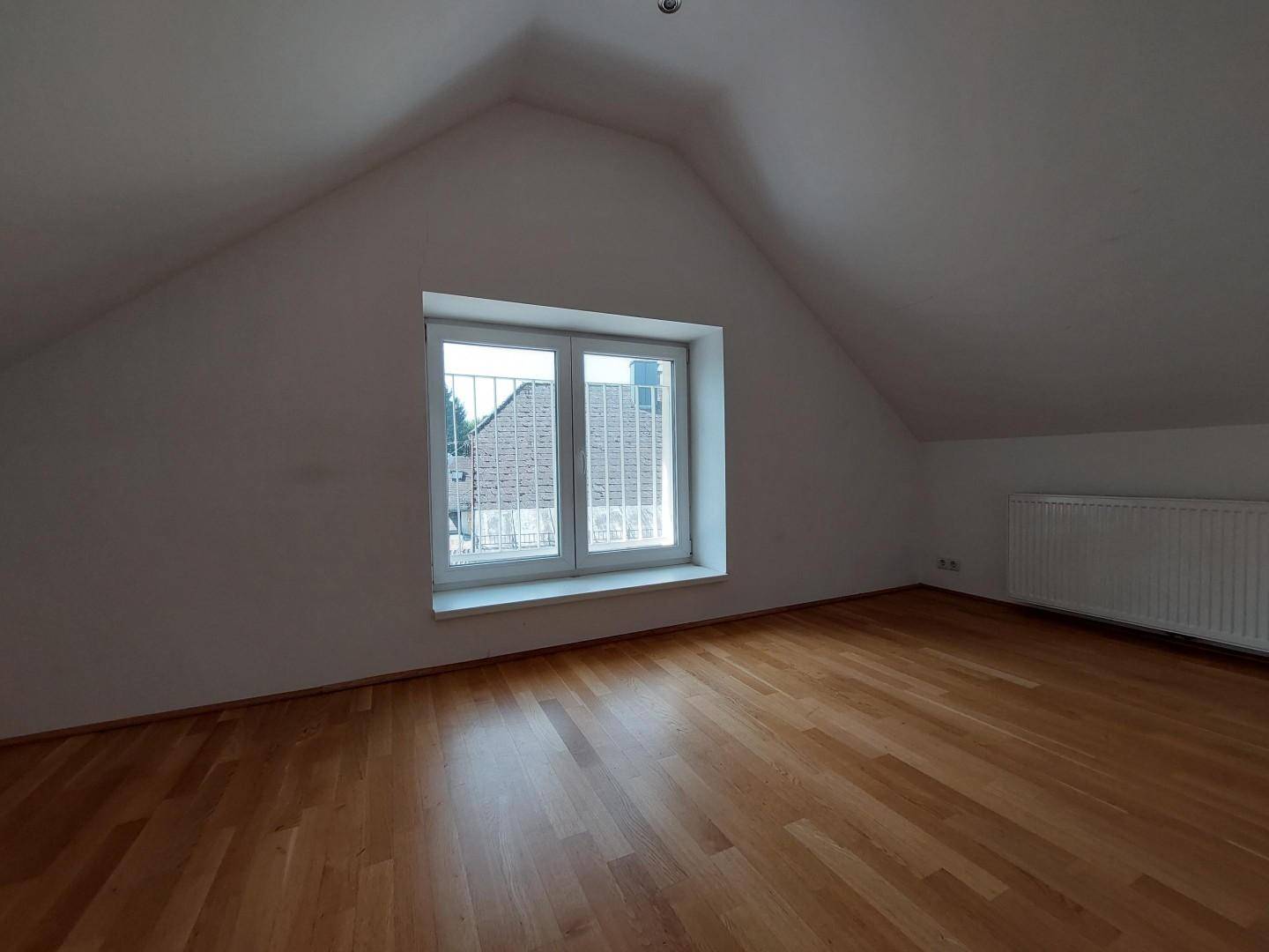 Gemütliches Schlafzimmer im Dachgeschoss mit schrägen Wänden, Parkettboden und Fenster.