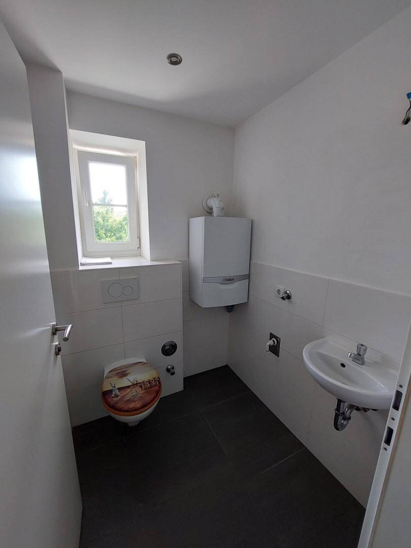 Kleines WC mit Fenster, Waschbecken und wandmontiertem Heizkessel.