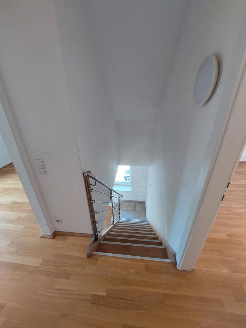 Holztreppe mit Metallgeländer, die in die untere Etage führt.