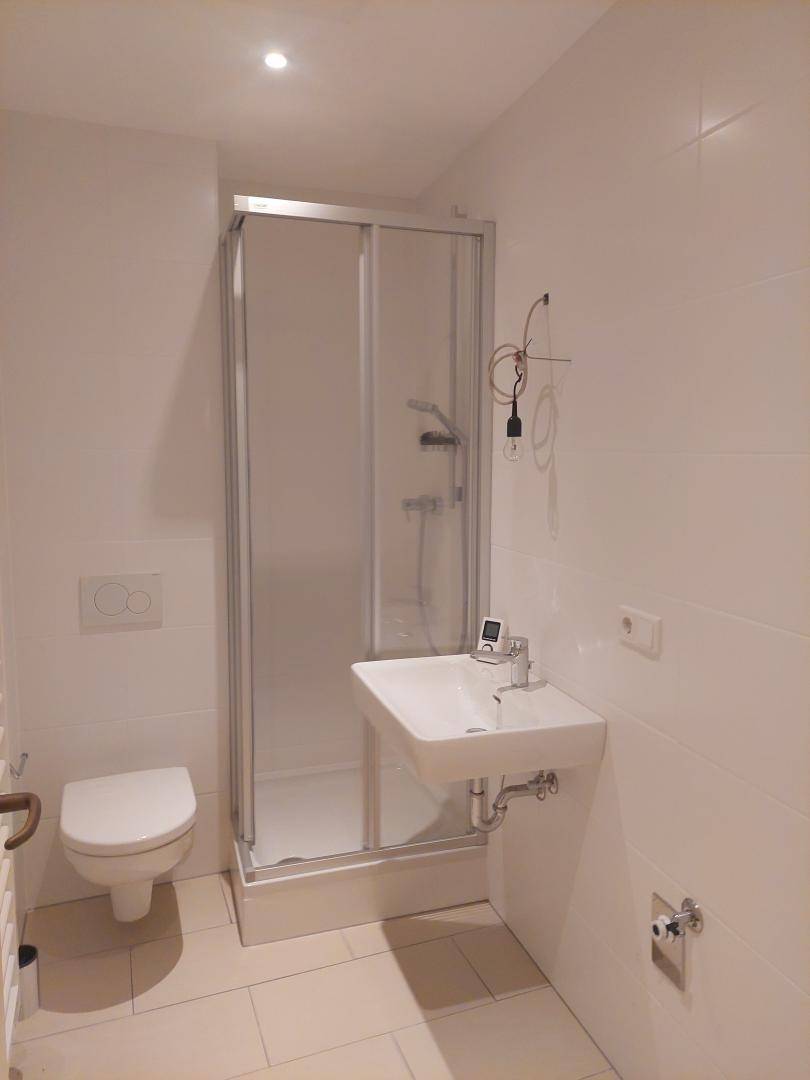 Kleines Badezimmer mit Dusche, WC und Waschbecken, komplett gefliest.