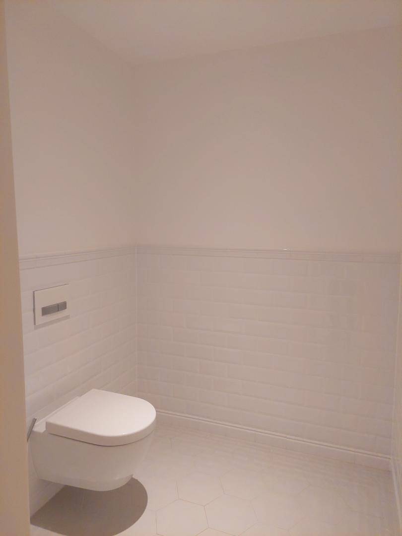 Separate Toilette mit Wand-WC und weißen Fliesen an den Wänden.