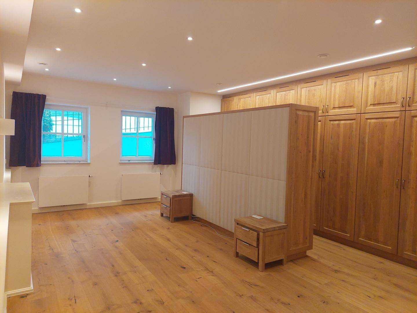 Großes Schlafzimmer mit Holzboden, Einbauschränken und zwei Fenstern.