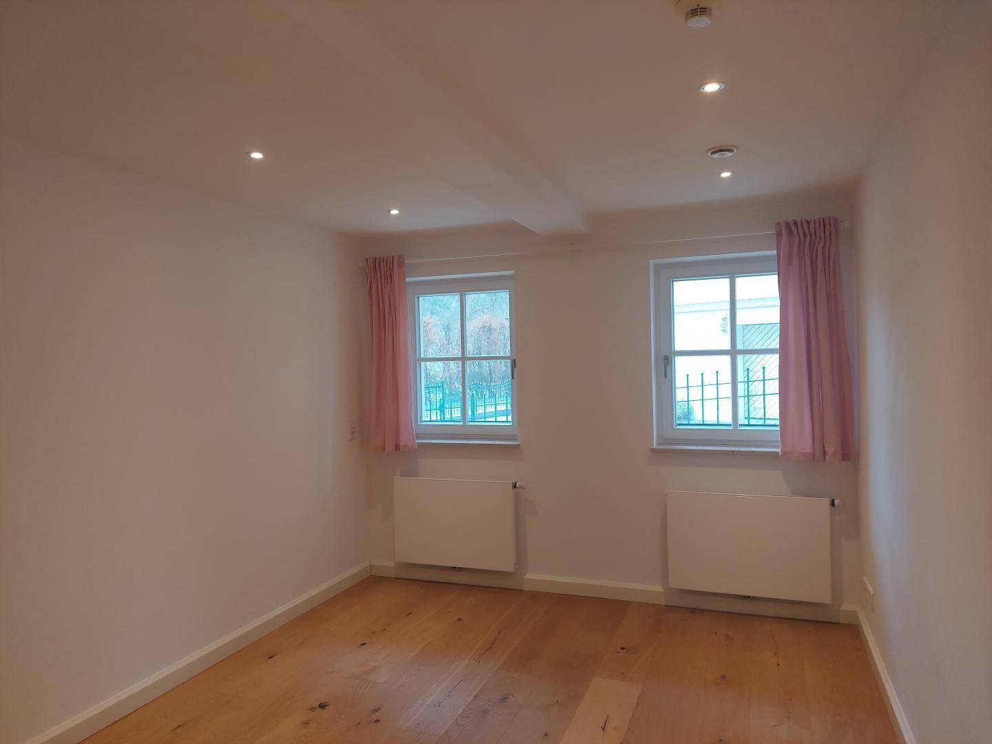 Helles Schlafzimmer mit Holzboden, zwei Fenstern und Einbaustrahlern in der Decke.