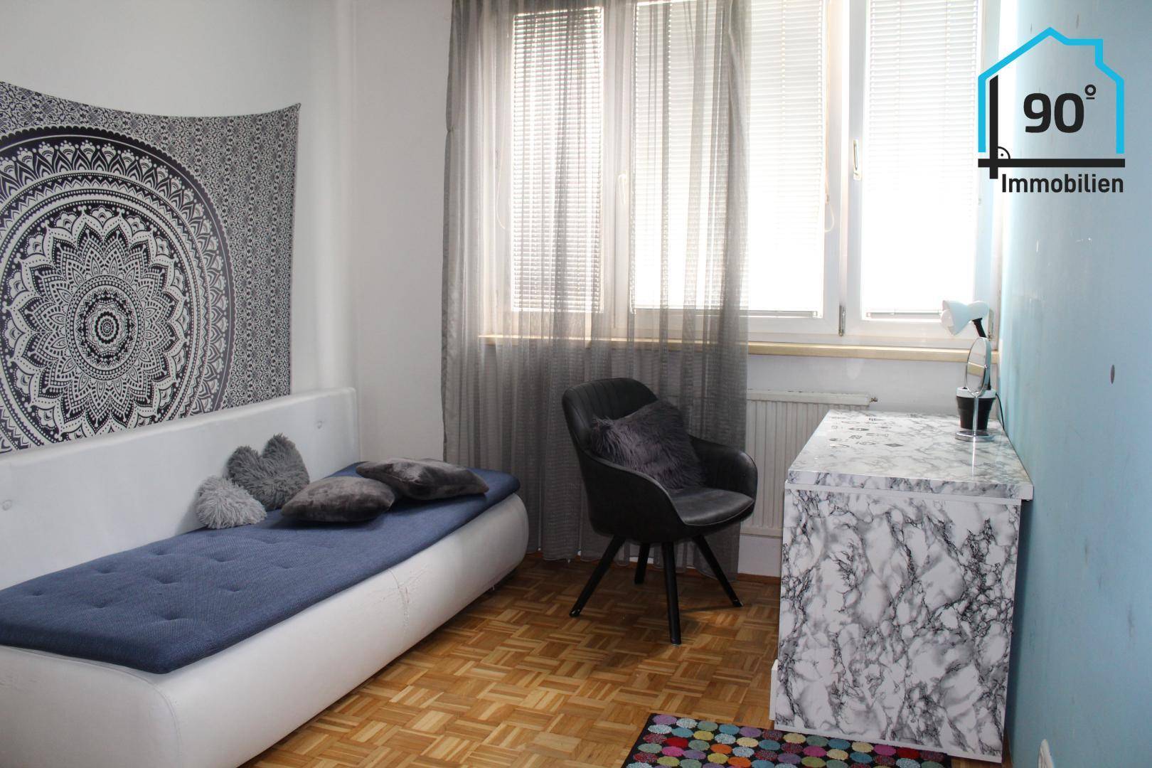Gemütliches Schlafzimmer mit Parkettboden, Tagesbett und einem dekorativen Wandteppich.