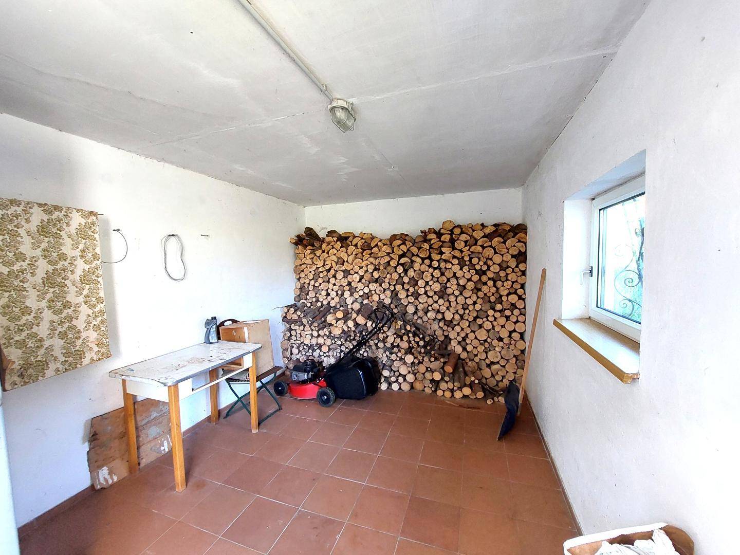 Geräumiger Abstellraum mit großem Holzstapel, Fliesenboden und Fenster.