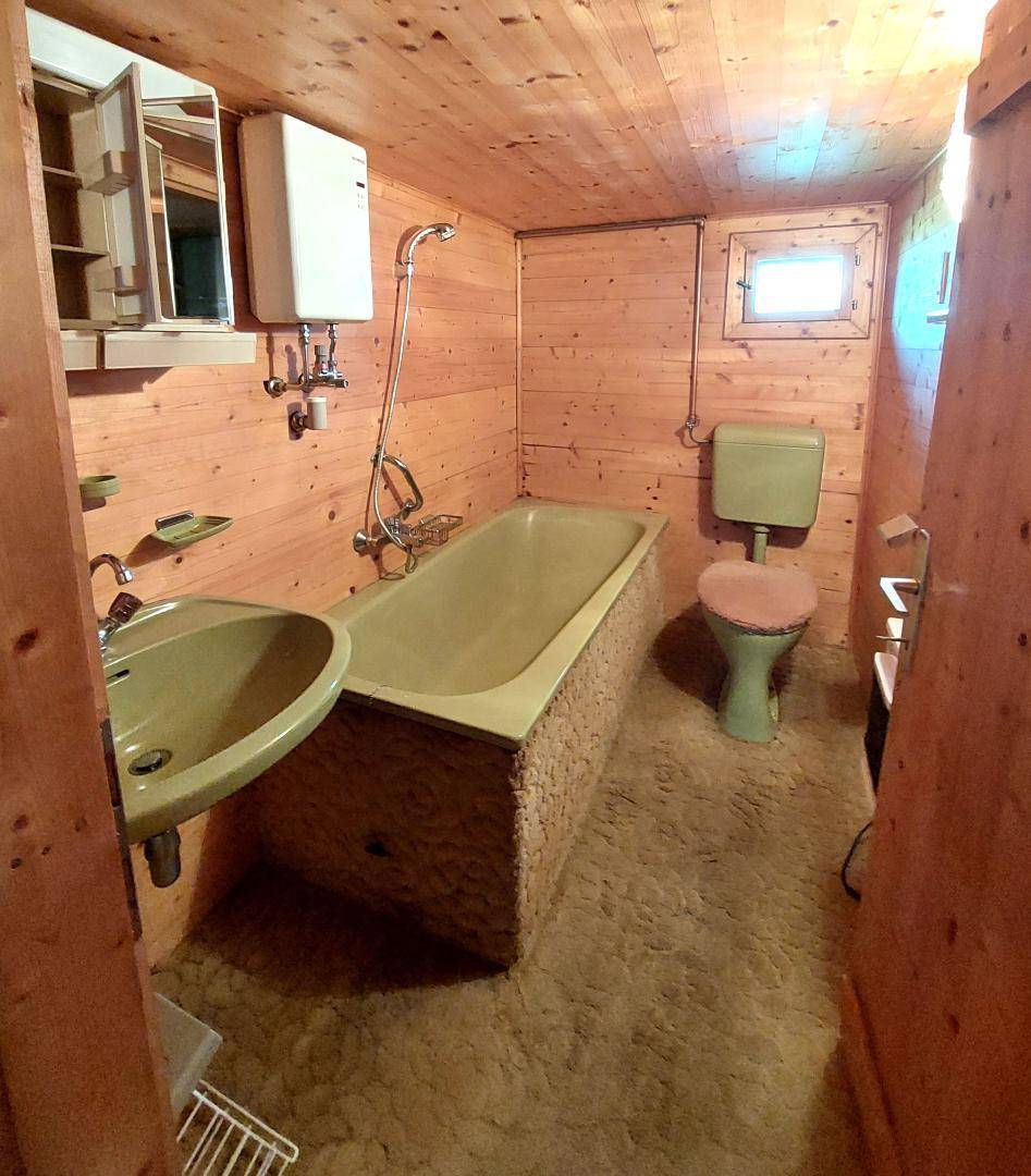 Badezimmer mit Holzverkleidung, Badewanne, Waschbecken und WC in einem älteren Zustand.