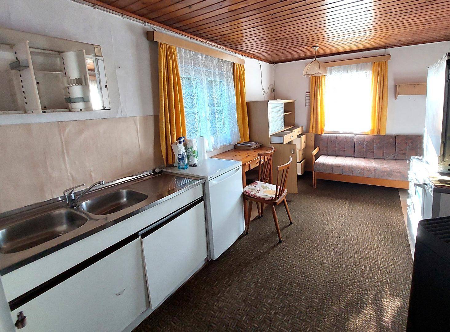Einfache Küchenzeile mit Spüle und Kühlschrank in einem Raum mit Teppichboden und Holzdecke.