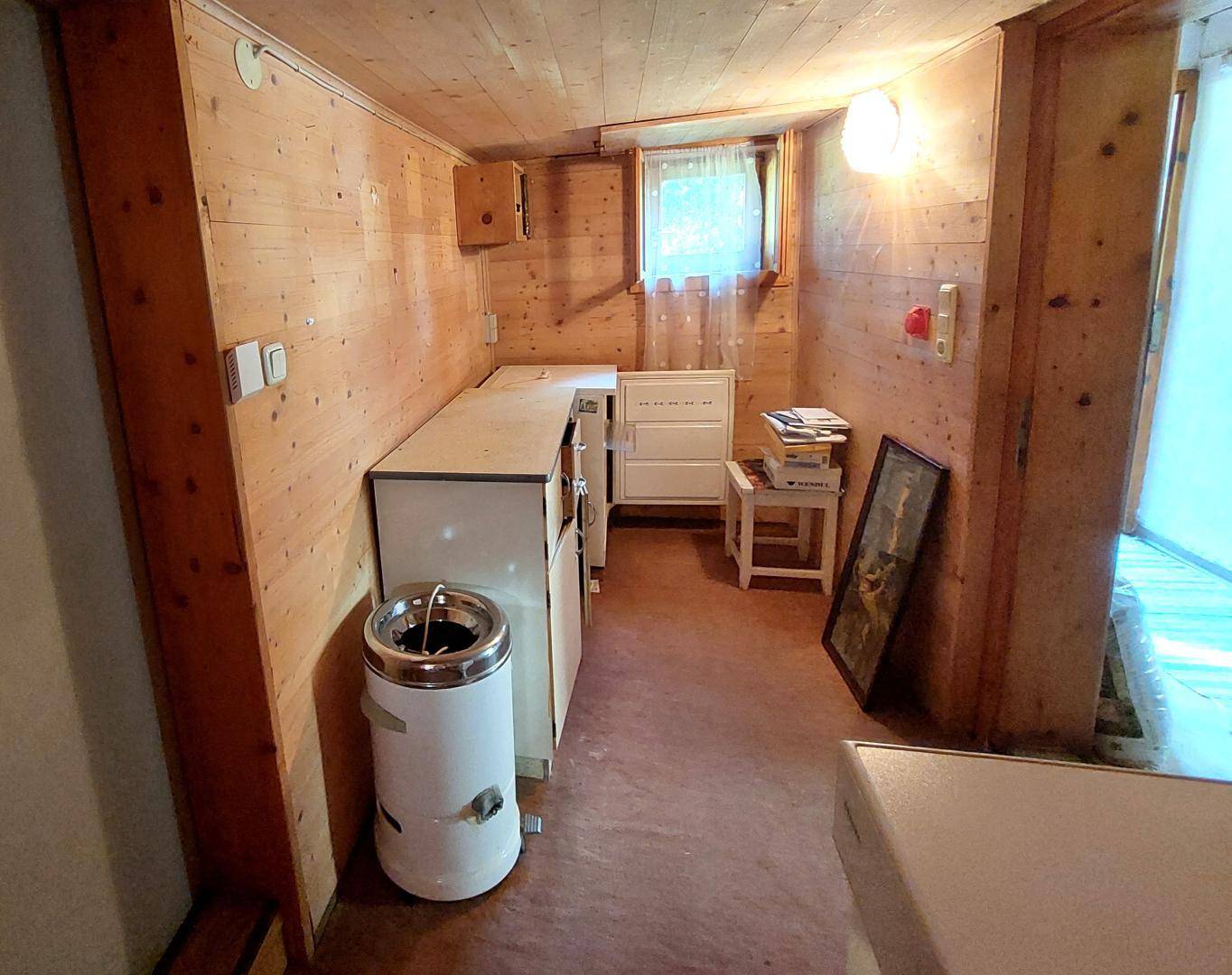 Raum mit Holzverkleidung, kleinem Schrank und Fenster, möglicherweise als Abstellraum genutzt.