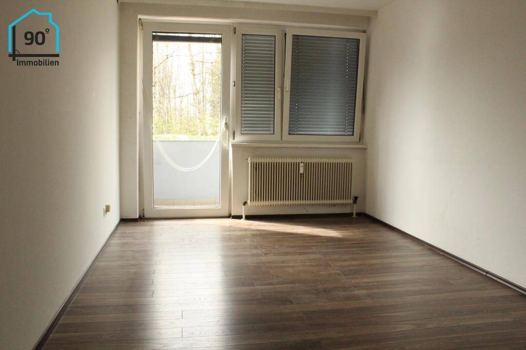 Helles Zimmer mit Laminatboden, Heizkörper und Zugang zu einem Balkon.