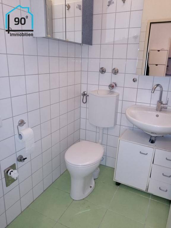Badezimmer mit WC, Waschbecken, Spiegelschrank und hellgrünen Bodenfliesen.
