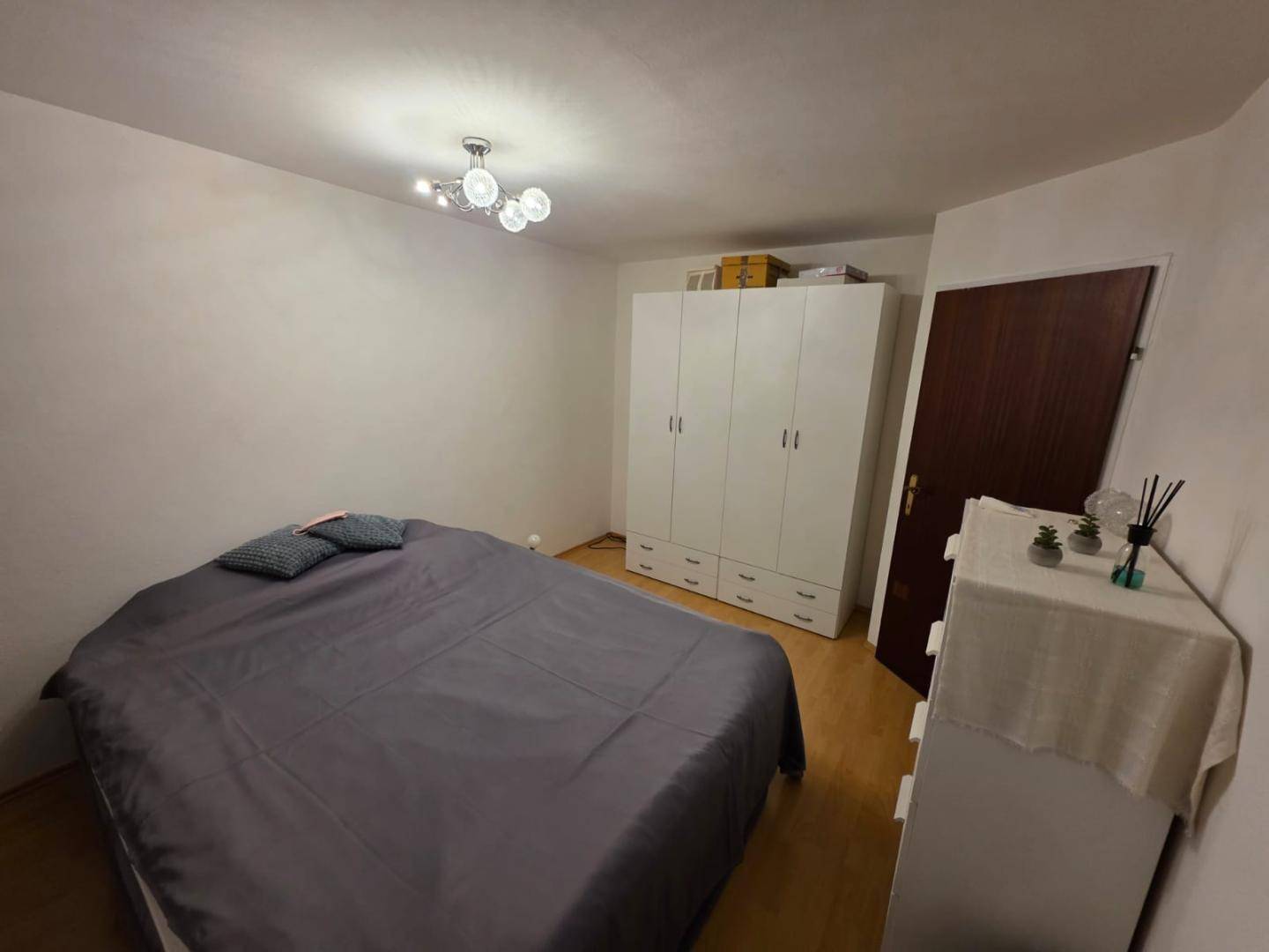 Schlafzimmer mit großem Bett, weißem Kleiderschrank und hellem Laminatboden.