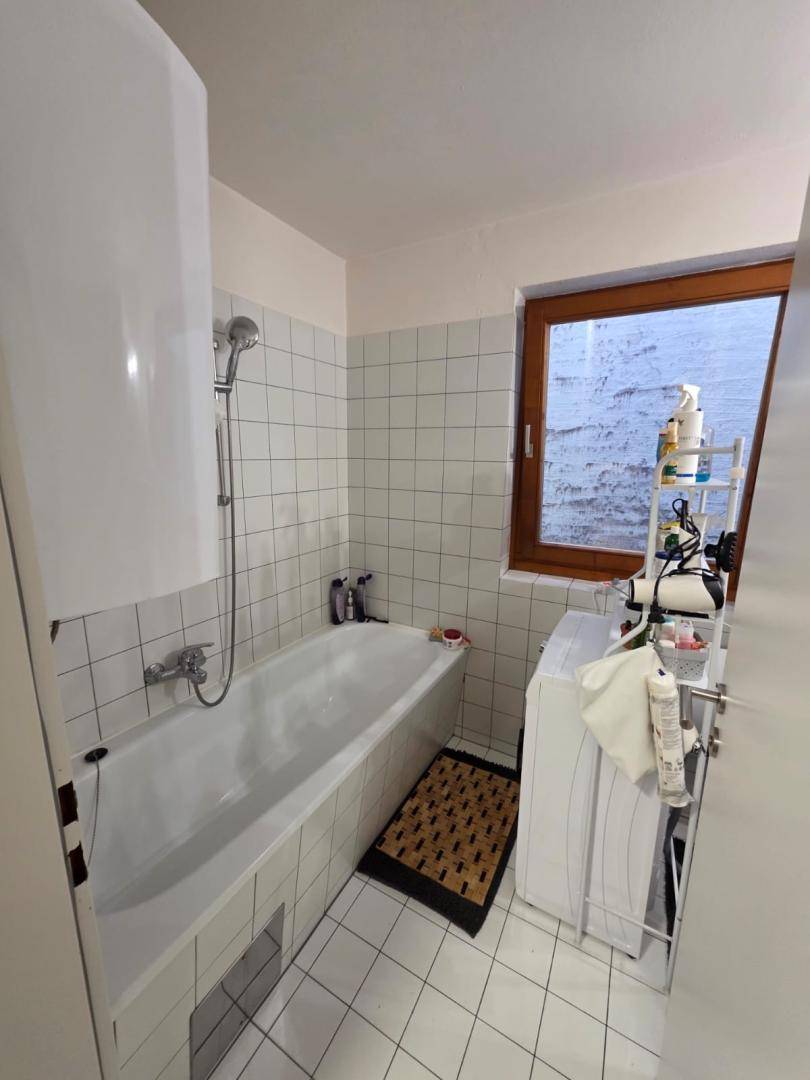 Badezimmer mit Badewanne, weißen Fliesen und einem Fenster für natürliche Belüftung.