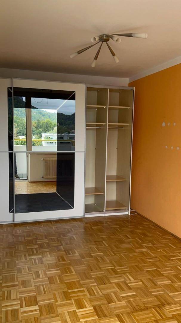 Schlafzimmer mit Parkettboden, großem Spiegelschrank und orangefarbener Akzentwand.