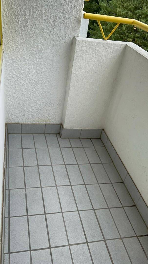 Kleiner Balkon mit grauen Fliesen und gelbem Geländer, umgeben von Bäumen.