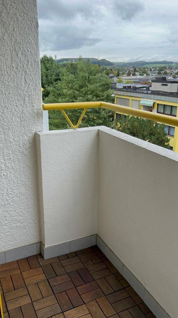Balkon mit Holzboden und gelbem Geländer, bietet einen weiten Blick ins Grüne.