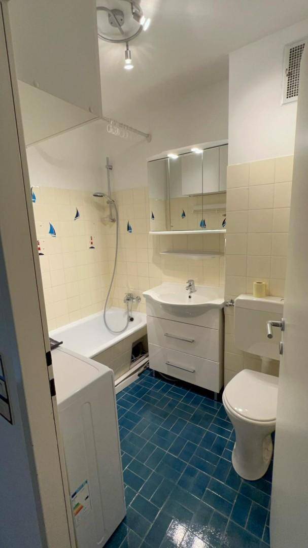 Badezimmer mit Badewanne, WC, Waschbecken und blauen Bodenfliesen sowie hellen Wandfliesen.