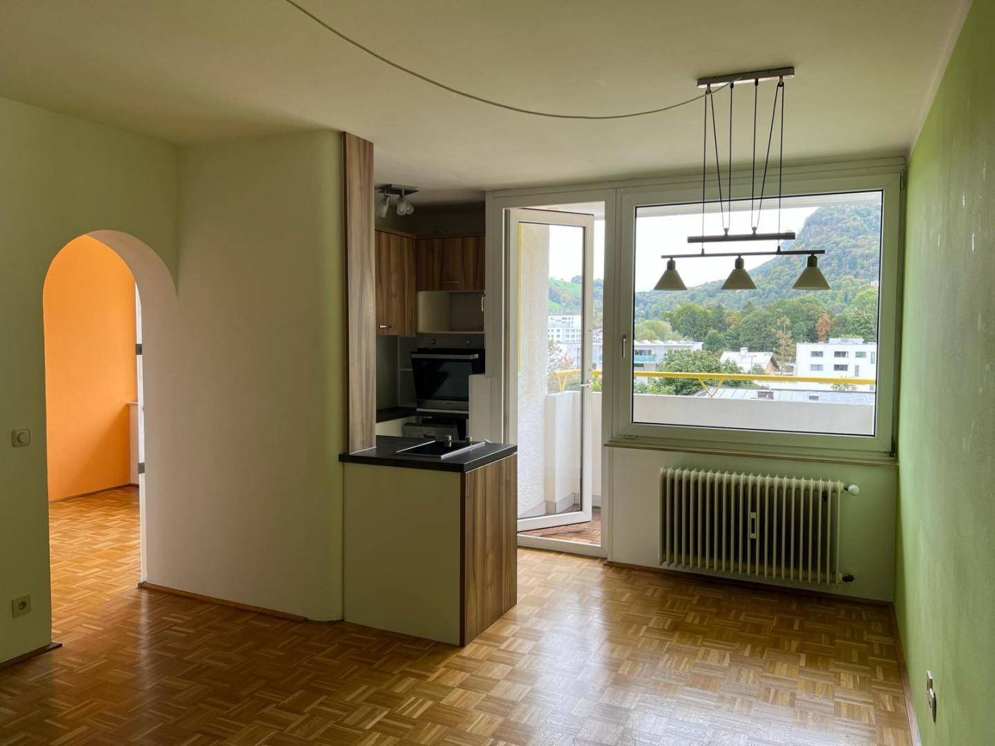 Offener Wohnbereich mit integrierter Küchenzeile, Parkettboden und Zugang zum Balkon.