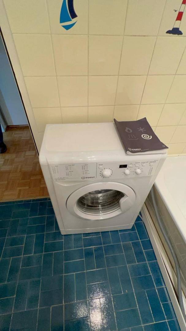 Waschmaschine im Badezimmer mit blauen Bodenfliesen und hellen Wandfliesen.