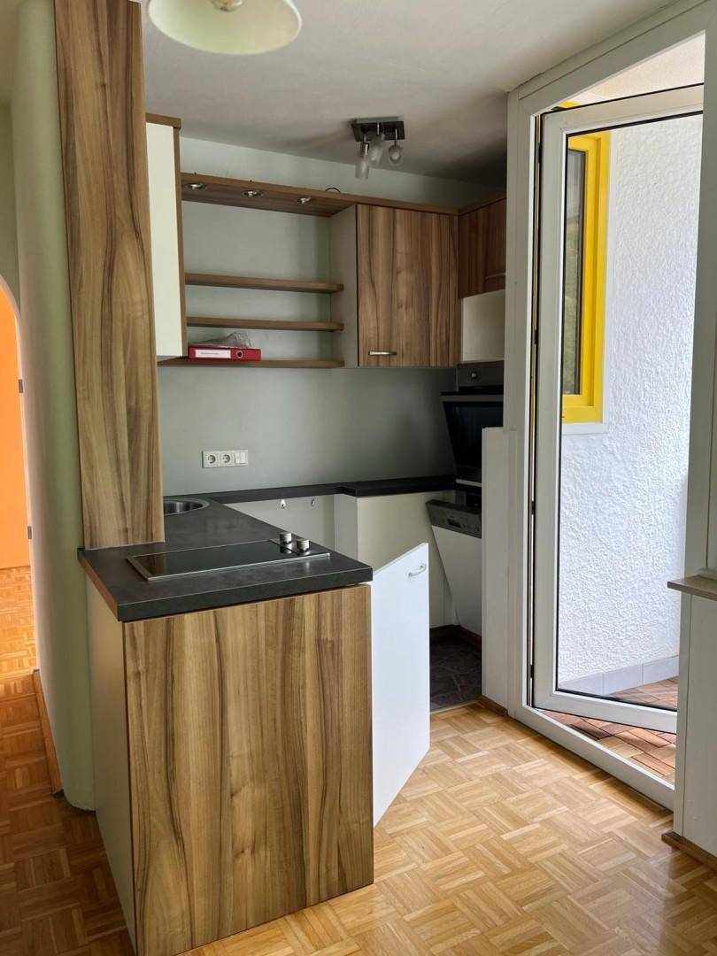 Kleine Küchenzeile mit Holzelementen, dunkler Arbeitsplatte und Zugang zu einem Balkon.
