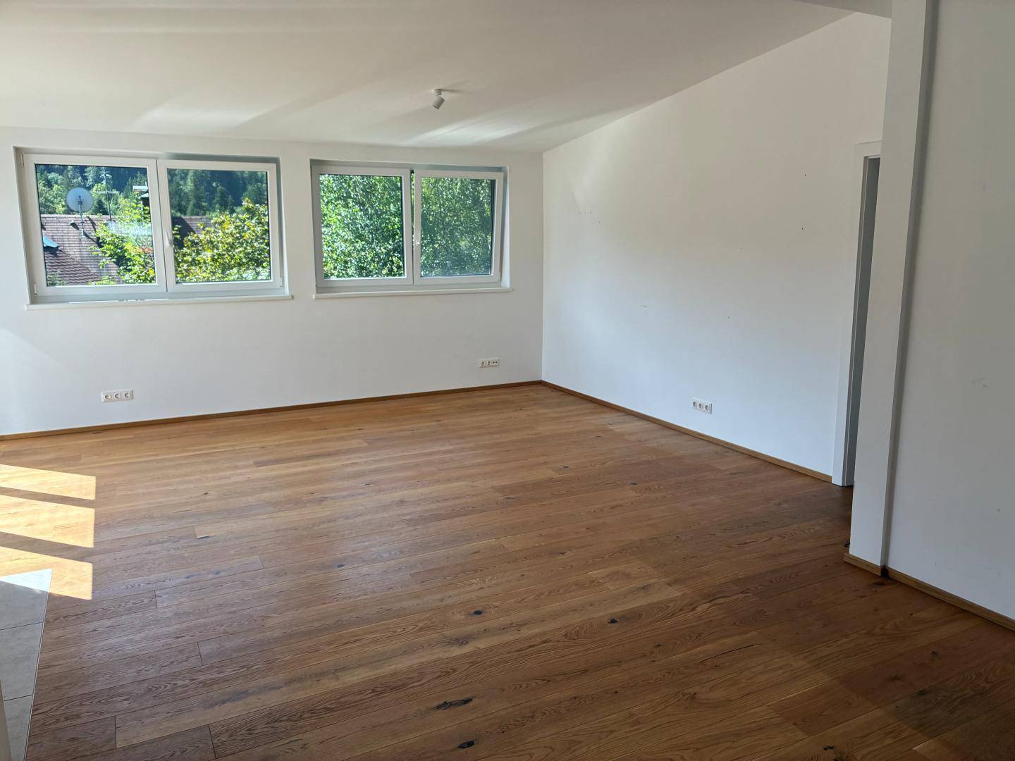 Großes, helles Wohnzimmer mit Holzboden und mehreren Fenstern, bietet viel Tageslicht.
