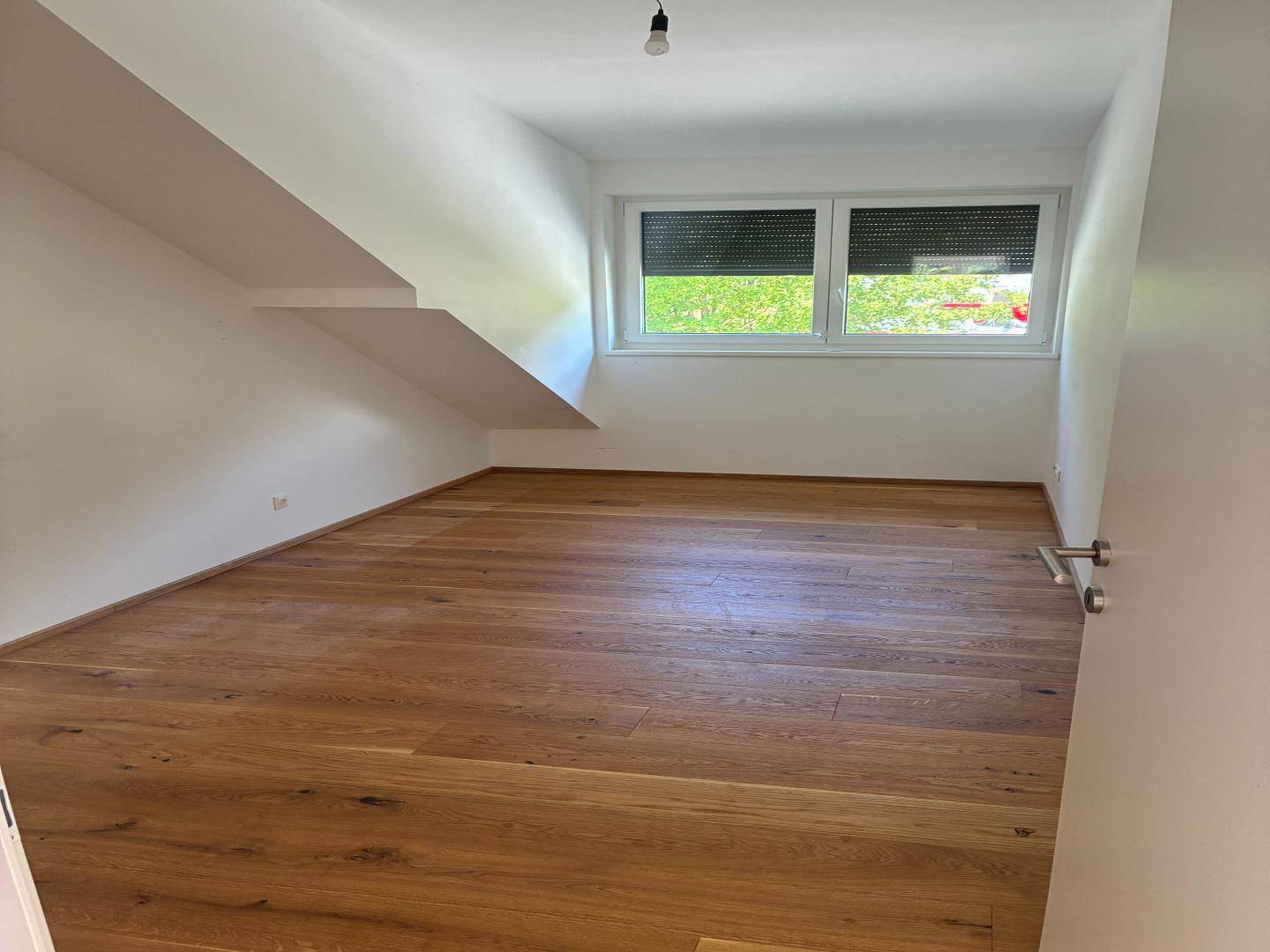 Geräumiges Zimmer mit Holzboden, Fenster und Dachschräge, bietet vielseitige Nutzungsmöglichkeiten.