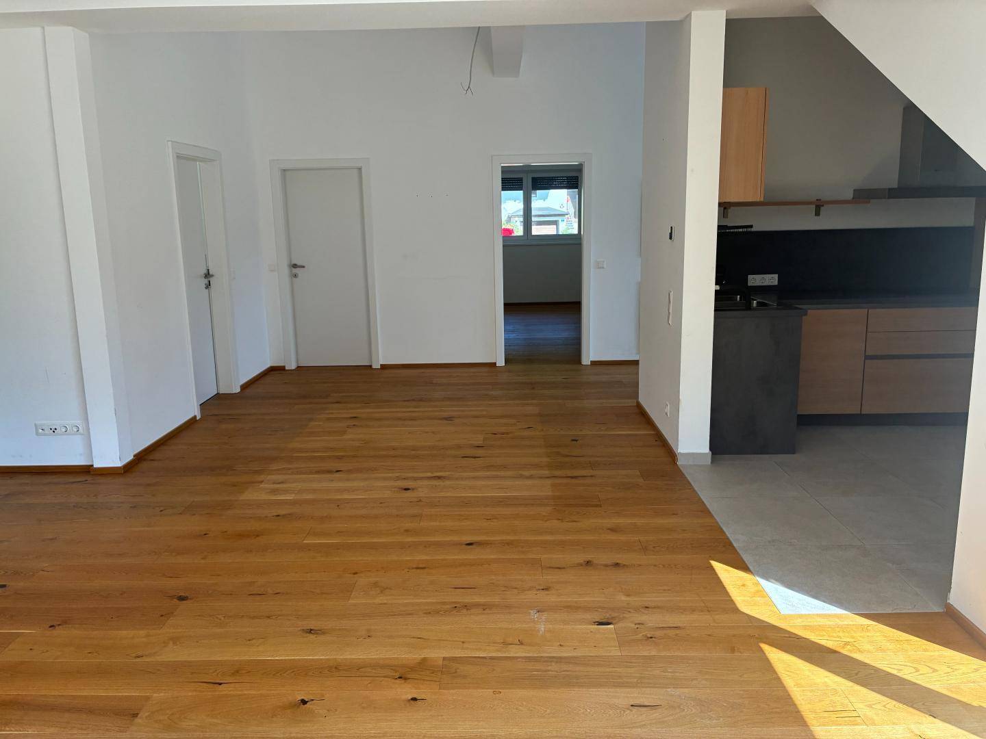 Offener Wohnbereich mit Holzboden, der in eine moderne Küche übergeht, ideal für geselliges Beisammensein.