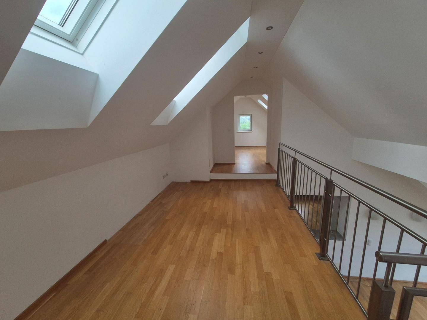 Heller Flur auf der oberen Etage mit Parkettboden, Dachfenstern und Blick in den unteren Bereich.